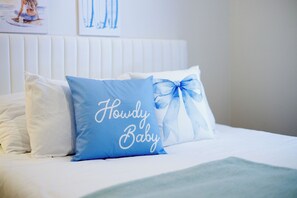 Ein Bett mit weißer Bettwäsche und einem blauen Kopfkissen mit der Aufschrift 'Howdy Baby'.