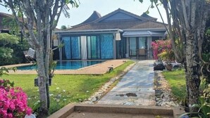 Una casa con piscina, un patio cubierto y un jardín con diversas plantas.