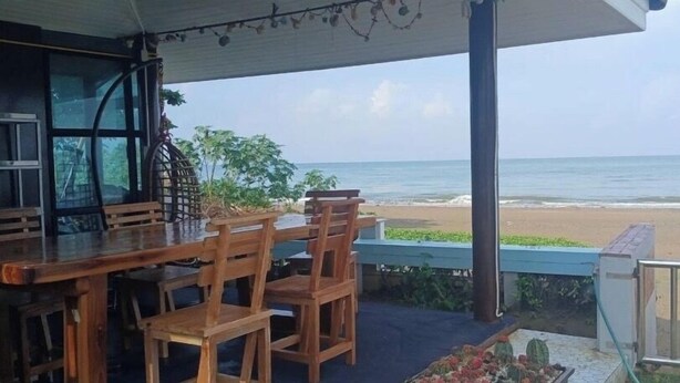 Mesa y sillas de madera en un balcón con vista a la playa.