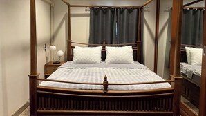 Una cama con dosel de madera y ropa de cama blanca, una mesita de noche con lámpara y un espejo en la pared.