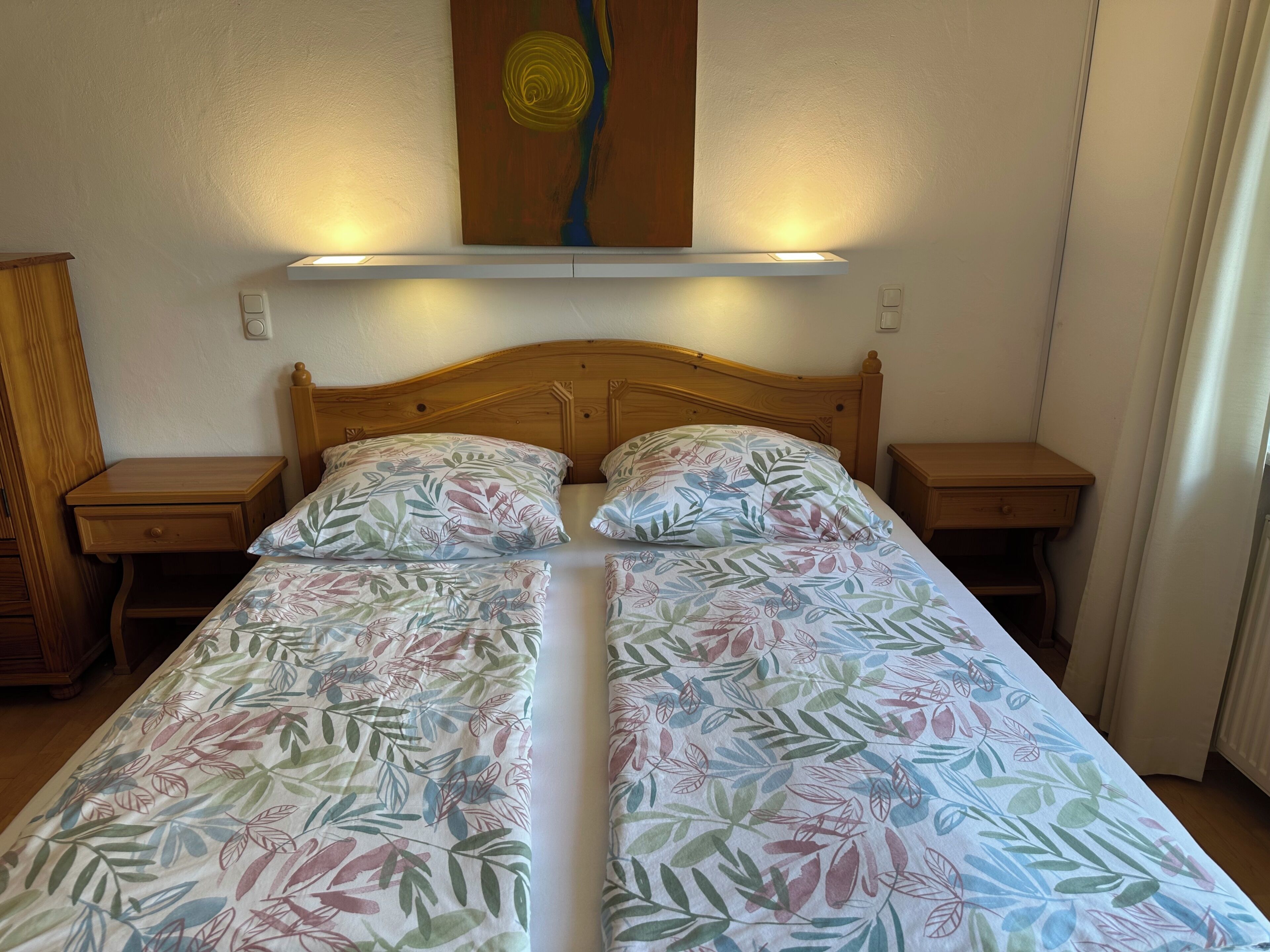 Een tweepersoonsbed met bloemenbeddengoed, een houten hoofdbord, nachtkastjes en een wandlamp.