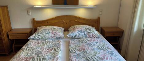 Een tweepersoonsbed met bloemenbeddengoed, een houten hoofdbord, nachtkastjes en een wandlamp.