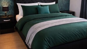 Ein Schlafzimmer mit dunkelbraunem Kopfteil, grünem Bettzeug, einer Nachttischlampe und einer Wand mit Muster.