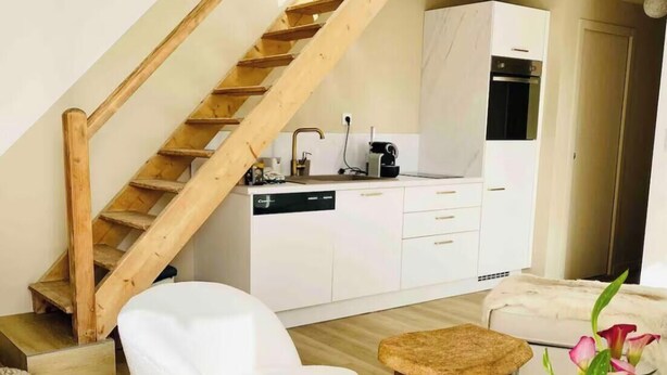Un interior moderno con una escalera de madera, cocina blanca, sofá blanco y una pequeña mesa redonda.