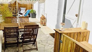 Un patio con una mesa y sillas, un banco de madera, un paraguas a rayas y una puerta blanca.