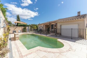 A swimming pool with a curved edge, a patio area with a tiled floor, and a building with a tiled roof. - Riad Provençale, with swimming pool, near a village located between sea and mountains. (Pertuis)