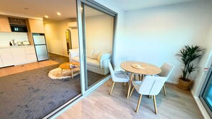 A modern interior with a dining area, a sofa, a kitchen, and a sliding glass door leading to a balcony. - Seaside Escape at New Brighton with Carpark (Christchurch)