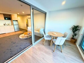 A modern interior with a dining area, a sofa, a kitchen, and a sliding glass door leading to a balcony. - Seaside Escape at New Brighton with Carpark (Christchurch)