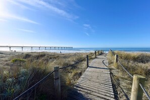 Ein hölzerner Steg führt zu einem Strand, im Hintergrund ist ein Steg zu sehen.