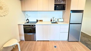 A compact kitchen with a built-in oven, a microwave, and a refrigerator. - Seaside Escape at New Brighton with Carpark (Christchurch)