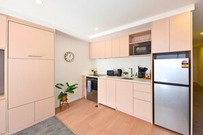 Une cuisine moderne avec des meubles de couleur bois clair, un réfrigérateur en acier inoxydable, un four à micro-ondes et un évier.