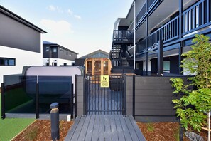 Un bâtiment moderne doté d’une entrée sécurisée par un portail, d’un escalier en bois et d’un petit jardin.