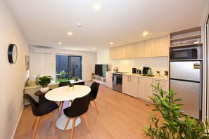 A modern kitchen with a dining area, built-in appliances, and a sliding glass door to a balcony. - Easy City Living near Christchurch CBD (Christchurch)