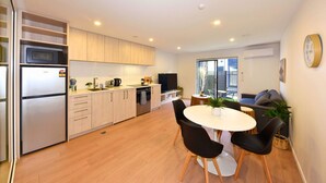A modern kitchen with a refrigerator, microwave, and stove, a dining area with a table and chairs, and a living area with a sofa and TV. - City Fringe Stay with Easy CBD Access (Christchurch)