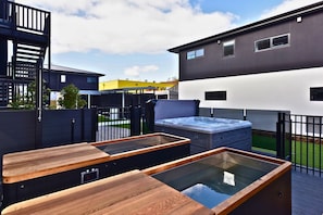 Eine moderne Terrasse im Freien mit Whirlpools, Holzliegen und blauem Himmel.