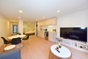 A modern apartment with a dining area, kitchenette, and a large TV.