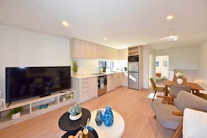 A modern living room with a flat-screen TV, a coffee table, and a dining area with a table and chairs. - Central Christchurch Base for Your Stay (Christchurch)