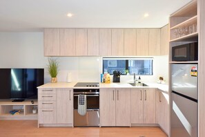 A modern kitchen with wooden cabinets, a built-in oven, a microwave, and a large window. - Central Christchurch Base for Your Stay (Christchurch)