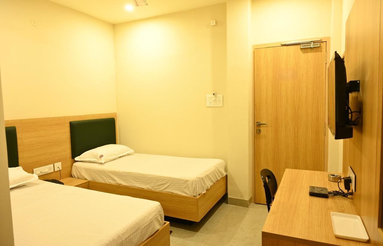 A hotel room with two single beds, a wooden desk, a chair, a TV mounted on the wall, and a door.