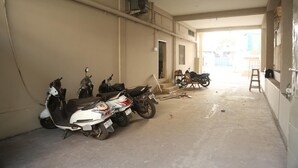 Un pasillo estrecho con suelo y paredes de concreto, algunos scooters estacionados contra la pared, y una escalera apoyada en la pared.
