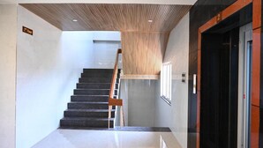 Un interior moderno con una escalera que sube al segundo piso, techo de madera y un ascensor negro.