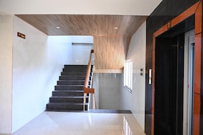 A modern interior with a staircase leading to the 2nd floor, a wooden ceiling, and a black elevator. - HOTEL SREE KANYA INN (Visakhapatnam)