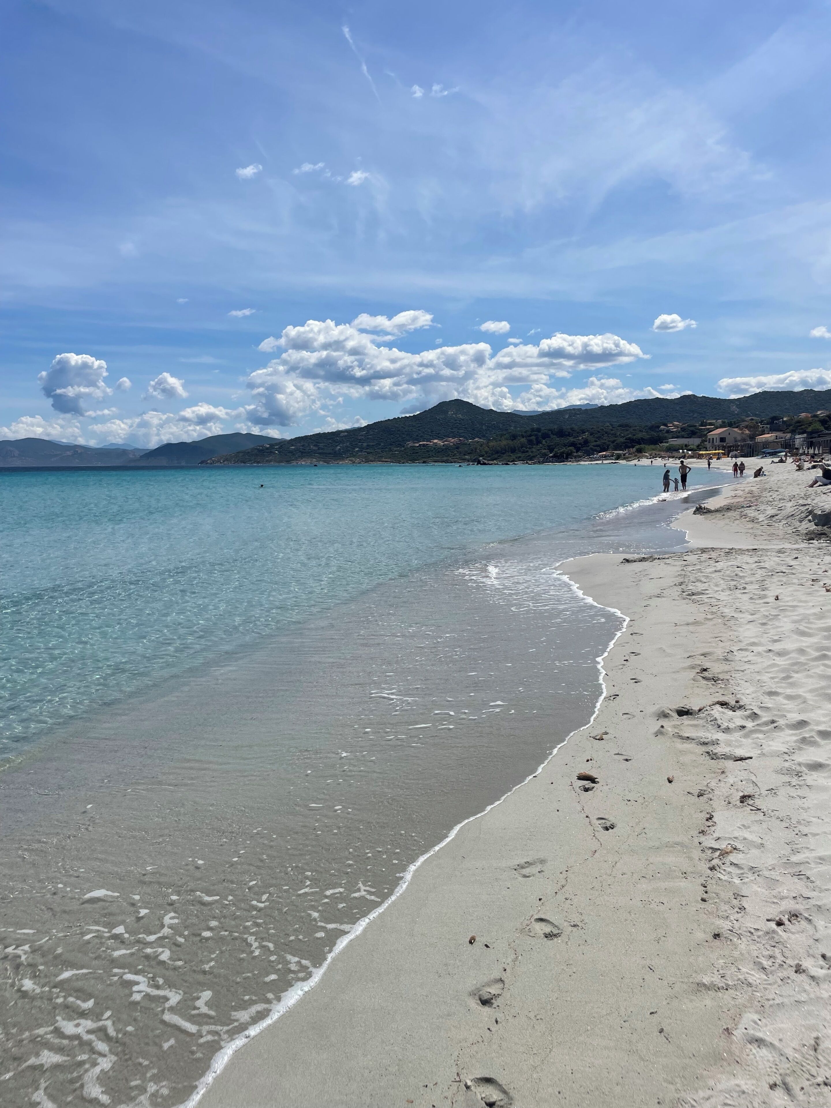 A beach with clear water, sandy shore, and distant hills.