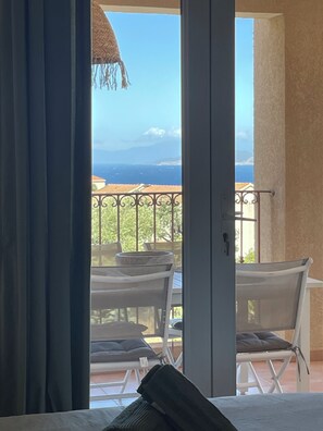 Ein Balkon mit Tisch und Stühlen, Blick auf das Meer und ein Reetdach.