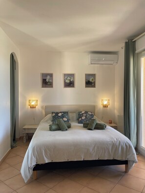 Uma cama com colcha listrada, duas almofadas, uma mesa de cabeceira, luminárias fixadas na parede e três quadros na parede.