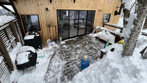 A wooden cabin with a covered patio, a sliding glass door, and a snow-covered deck. - Walk to Tsugaike Ski Resort 200m. Floor heating, driveway heating, cosy & unique (Otari)