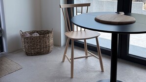 A corner room with a round table, a wooden chair, a wicker basket, and a view of a green landscape through a large window. - Tiny house near Hameln—in a quiet, rural setting in the Weserbergland region! (Hessisch Oldendorf)