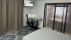 Hotellihuone, jossa on sänky, työpöytä tuolilla, seinälle asennettu televisio, ilmastointilaite ja liukuovi.