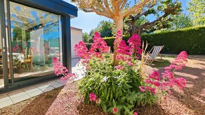 A modern building with large glass windows, a garden with pink flowers, and a wooden deck. - La Pause Jardaise near beaches (Jard-sur-Mer)