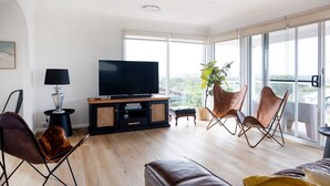 Una sala de estar moderna con televisor de pantalla plana, sillones de cuero, piso de madera y ventanas amplias con vistas.
