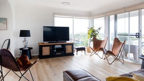 Ein modernes Wohnzimmer mit Flachbildfernseher, Ledersesseln, Holzboden und großen Fenstern mit Blick.