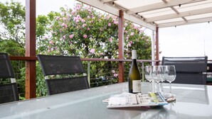 Una mesa con una botella y copas, un menú, y vistas a flores rosadas y follaje.