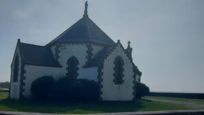 Eine Kirche mit spitzem Dach, Rundbogenfenstern und einem Kreuz auf der Spitze.