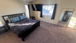 A bedroom with a bed, a TV mounted on the wall, a window with curtains, and a mirror.
