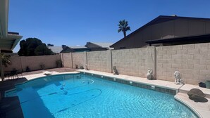 A clear blue swimming pool with a curved edge, surrounded by a brick wall and a palm tree in the background.