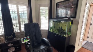 A room with a massage chair, a fish tank, and a television on the wall.