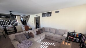 A living room with a sectional sofa, a coffee table, a bookshelf, and a staircase leading to another level.