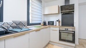 A modern kitchen with a built-in oven, a microwave, and a window with blinds. - Ker Marin - Maison Le Refuge Des Marées: terrace, garden & Wi-Fi (Sarzeau)