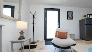 A modern living room with a sofa, a lamp, a coat rack, a refrigerator, and a door leading outside. - Ker Marin - Maison Le Refuge Des Marées: terrace, garden & Wi-Fi (Sarzeau)
