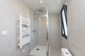 Une salle de bain moderne avec une douche à parois de verre, un porte-serviettes blanc et une fenêtre.