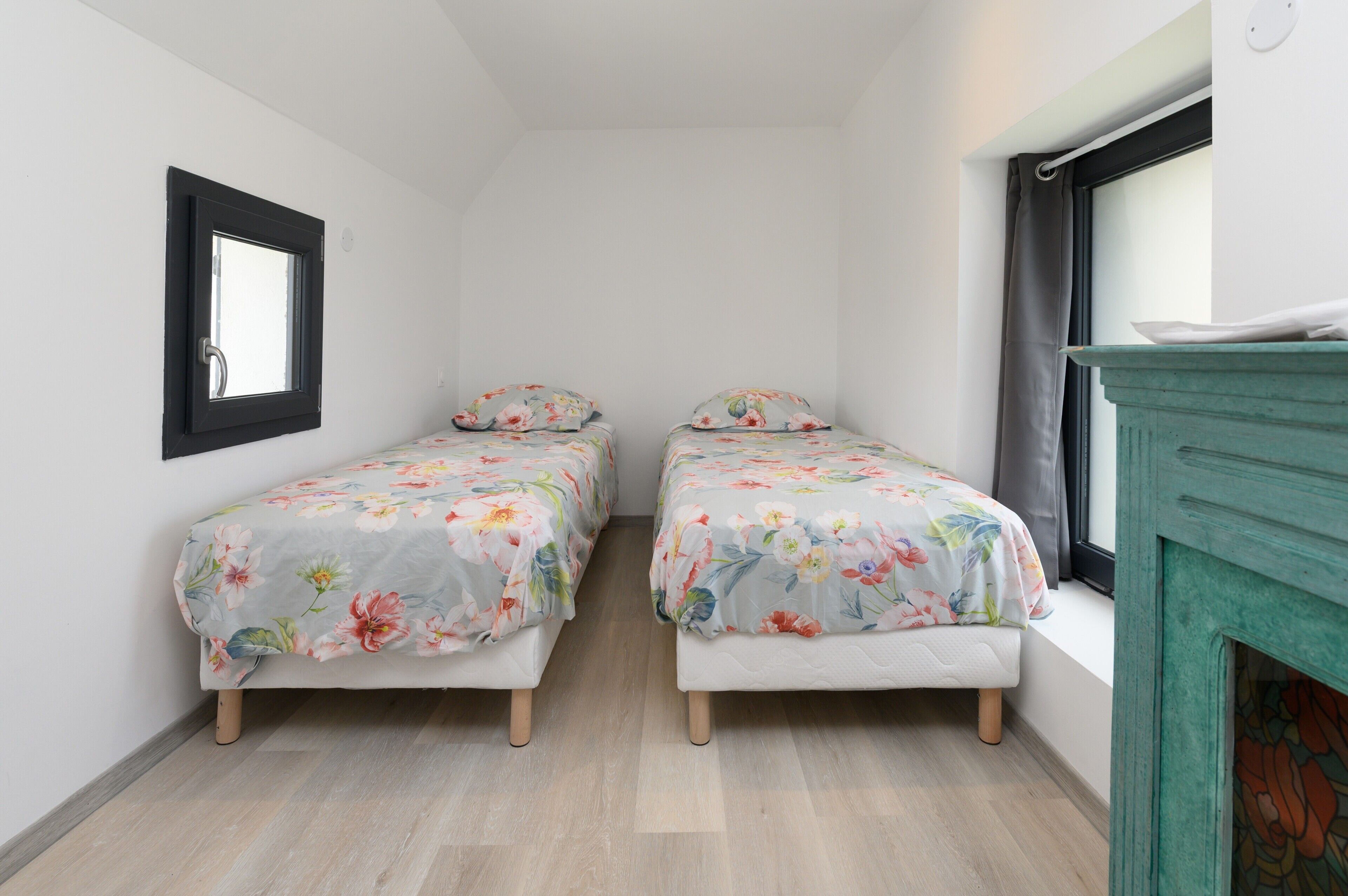 A small room with two single beds, a mirror on the wall, and a fireplace.