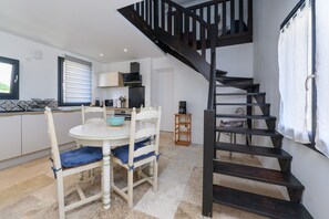 A kitchen with a dining table, chairs, a staircase, and a window with blinds. - Ker Marin - Maison Le Refuge Des Marées: terrace, garden & Wi-Fi (Sarzeau)