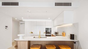 A modern kitchen with a central island, bar stools, and built-in appliances. - The Coastal Luxe Haven, Coolangatta (Gold Coast)