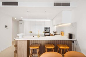 A modern kitchen with a central island, bar stools, and built-in appliances. - The Coastal Luxe Haven, Coolangatta (Gold Coast)