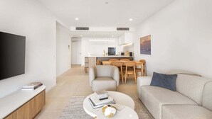 A modern living room with a flat-screen TV, a sofa, a coffee table, and a dining area with chairs and a table. - The Coastal Luxe Haven, Coolangatta (Gold Coast)