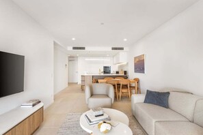 A modern living room with a flat-screen TV, a sofa, a coffee table, and a dining area with chairs and a table. - The Coastal Luxe Haven, Coolangatta (Gold Coast)